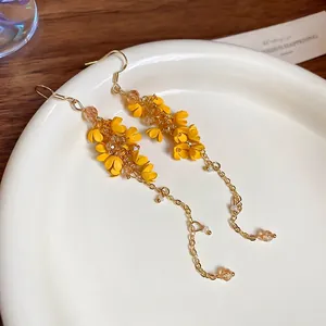 Elegant yellow floral tassel earrings with gold chains and crystal beads on white ceramic