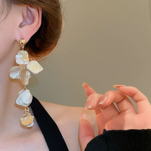 Close-up of golden shell fringe earrings worn by a model, showing elegant tassels