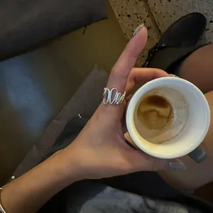 Close-up of minimalist irregular wave silver ring worn by a model holding a cup