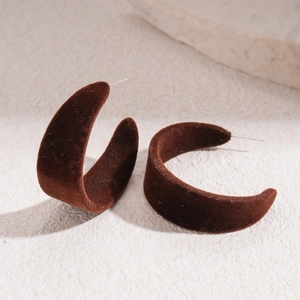 Detailed view of brown velvet C-shape earrings on a textured stone surface