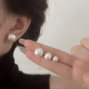 Detail showing three sizes of white freshwater pearl earrings on model ear for comparison