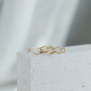 Detailed close-up of slim gold wavy stackable rings on a white stone display pedestal