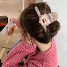 Close-up of soft plush hair clip featuring embroidered red cherries and floral patterns