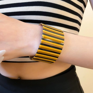 Detail of wide acrylic open cuff bracelet featuring striped yellow and brown patterns