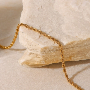 Detailed macro shot of 2mm gold twisted rope chain anklet on a textured stone base