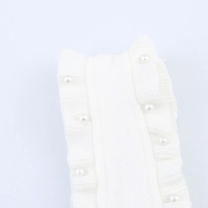 Detail of white ribbed knit fabric featuring ruffled edges and elegant pearl decorations