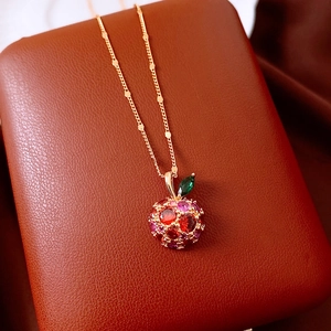 Macro view of 14k gold apple pendant with red pavé stones and green leaf detail