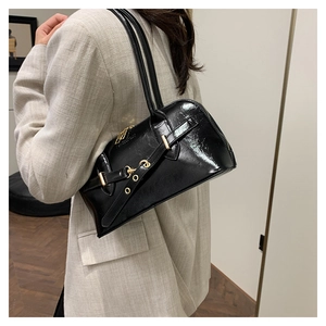 Detail of black patent leather underarm bag featuring glossy finish and gold metal buckle