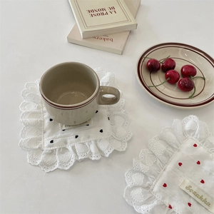 Close-up of white lace placemat with heart embroidery under a ceramic coffee cup