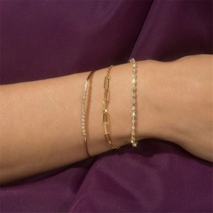 Close-up of stacked gold paperclip chain, tennis bracelet and pavé cuff on wrist