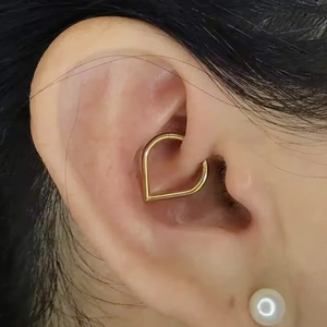 Close-up of golden heart-shaped G23 titanium daith piercing ring on a model ear