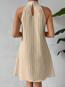 Detail of halter neck beige pleated dress featuring back cutout and double button closure