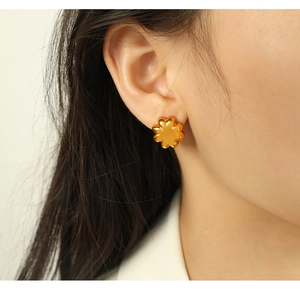 Close-up of golden flower stud earrings in a six-petal design worn on ear with high detail