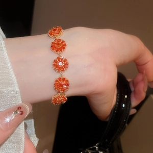 Close-up of 18k gold-plated bracelet with orange zircon floral charms on woman's wrist