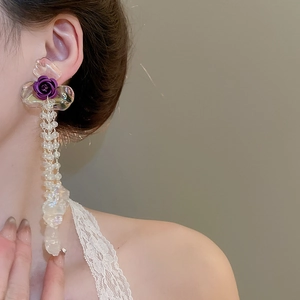 Detailed view of long floral drop earrings with purple roses and clear crystal beads