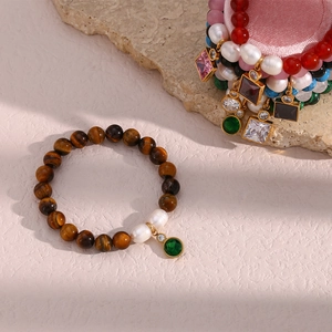 Detail of tiger eye bead bracelet with pearls and green gemstone pendant in macro view