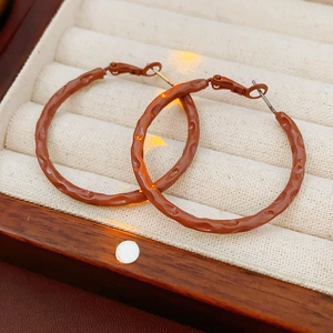 Macro detail of brown hoop earrings featuring a vintage hammered metal texture on velvet