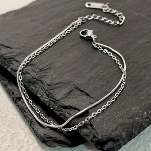 Minimalist silver double layer snake and link chain bracelet on a dark stone background
