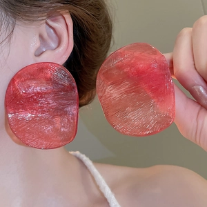 Detail showing oversized translucent red resin earrings with unique textured finish