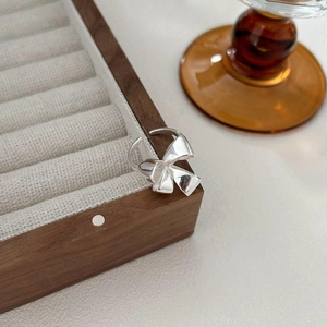 Macro shot of silver bow heart ring with adjustable open band on wooden display box