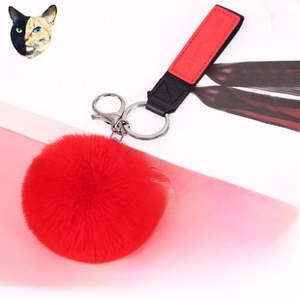 Detail of red faux fur pompom keychain with a black and red leather strap and metal clasp