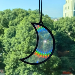 Detail of crescent moon suncatcher with prism effect reflecting rainbow light on window