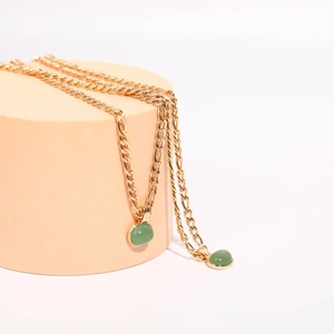 Detail of green aventurine oval pendants on a gold Figaro chain over a peach pedestal