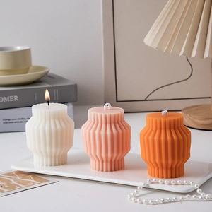 Three geometric scented candles in white, pink, and orange with stylish paper-fold textures
