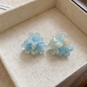 Macro detail of blue and white floral resin stud earrings inside a rustic wooden box