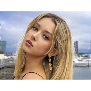 Detail of gold spiral disc pendant earrings on a model with a scenic harbor backdrop