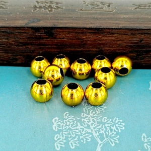 Polished gold plated pumpkin beads for DIY jewelry making on textured fabric background