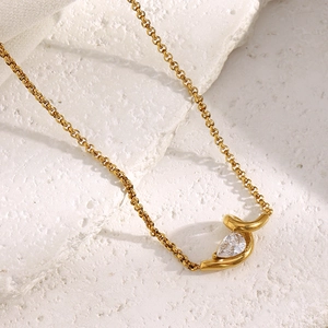 Detail of 18K gold plated necklace featuring a teardrop zircon and pearl on a textured stone