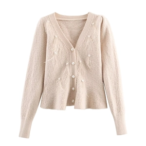 Detailed close-up of cream knit cardigan featuring pearl buttons and soft feather accents