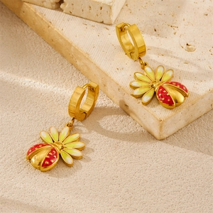Détail de boucles d'oreilles coccinelle et fleur en émail rouge et finition dorée
