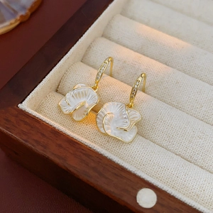 Close-up of gold flower earrings with white mother-of-pearl in a beige suede jewelry box