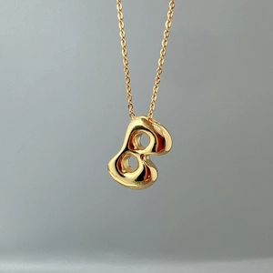 Detailed close-up of polished gold necklace with abstract figure-eight pendant on a fine chain
