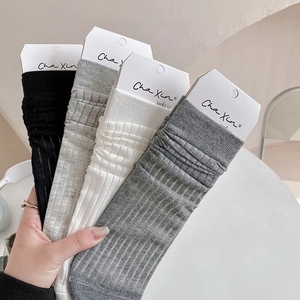 Close-up of four pairs of ribbed cotton socks in black, white, and grey with card packaging