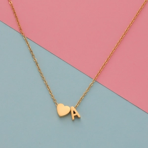 Golden stainless steel heart necklace with letter A pendant on a pink and blue background