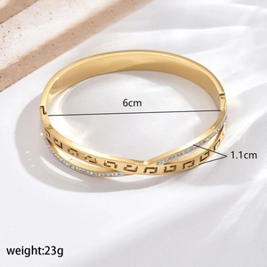 Detail of gold crossover bangle with Greek fret pattern and clear crystals on white fabric