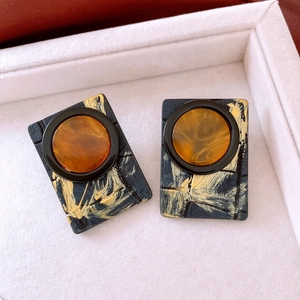 Detailed macro view of black square leather earrings with gold texture and amber resin core