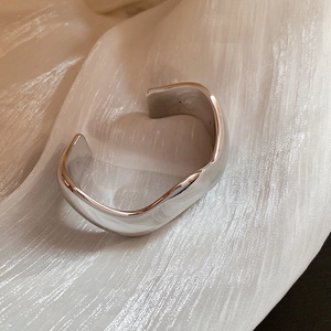 Dettaglio ravvicinato di un bracciale a polsino d'argento ondulato su tessuto di seta beige