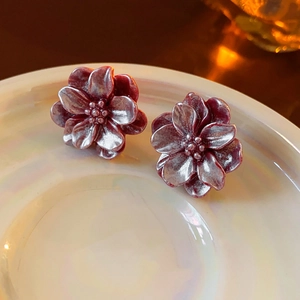 Gros plan détaillé des boucles d'oreilles fleurs doubles bordeaux mat sur un plateau