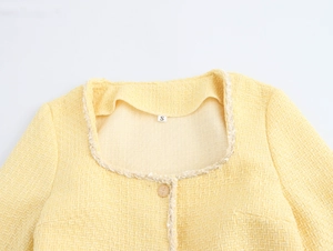 Detail of yellow tweed dress with square neckline, fringe trim and golden button