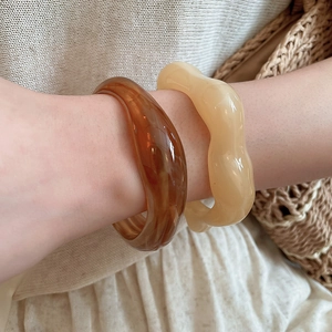 Detail view of wave-shaped acrylic rings in amber and cream with a glossy finish