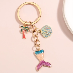 Mermaid tail keychain with palm tree and shell charms on a soft pink background