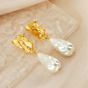 Macro detail of irregular gold metal earrings with baroque teardrop pearl pendants