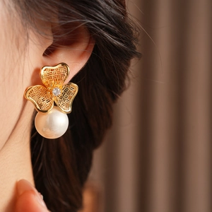 Macro shot of gold clover earrings with sparkling zircon and elegant hanging white pearl