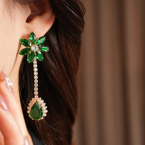 Close-up of elegant gold tassel earrings with green crystal flower and teardrop pendants