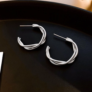 Detailed view of silver twisted hoop earrings with a woven braided texture on a black tray