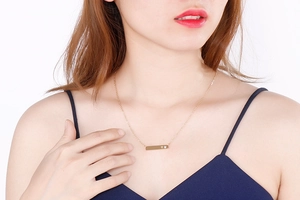 Detail of a gold bar necklace with heart engraving and crystal on model's neck